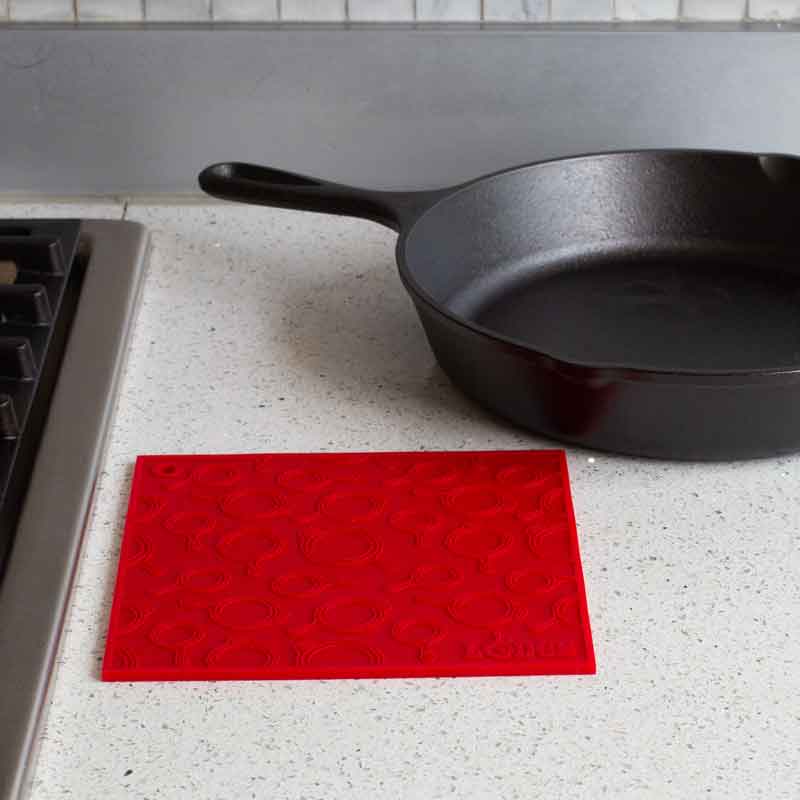 Red silicone trivet placed flat on counter next to stove and skillet.