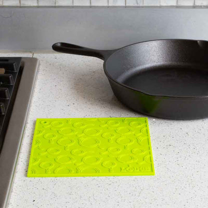 Green silicone trivet placed flat on counter next to stove and skillet.
