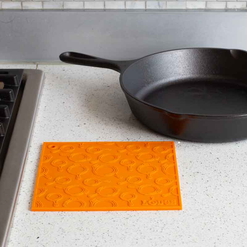 Orange silicone trivet placed flat on counter next to stove and skillet.
