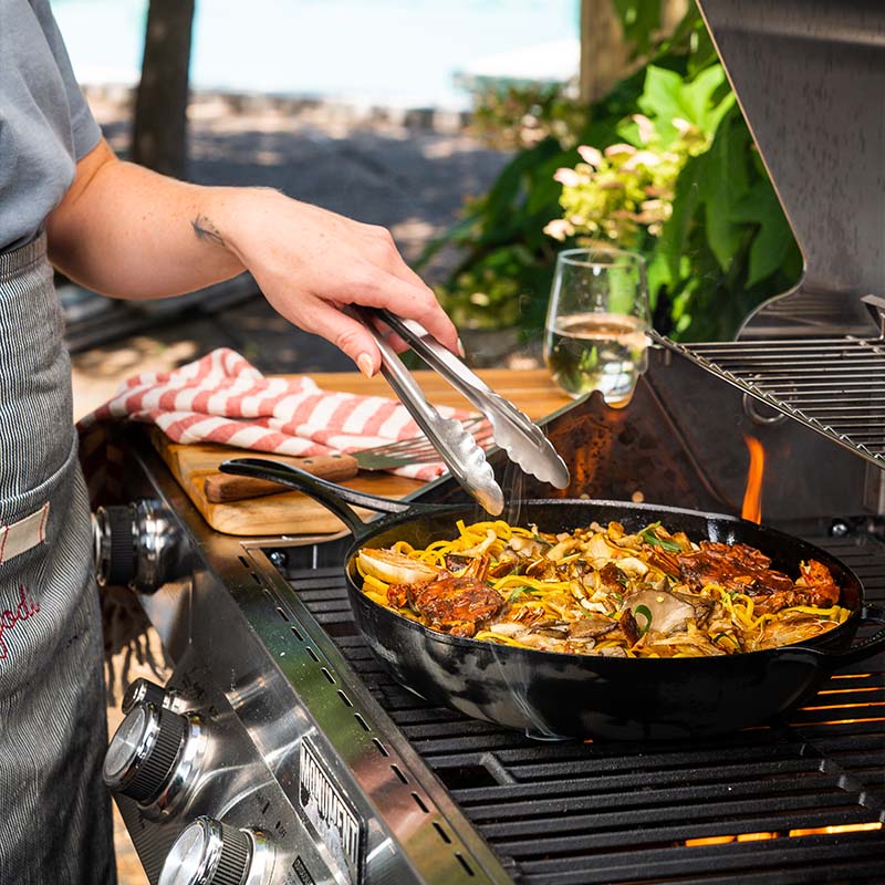 Someone cooking with skillet on grill.