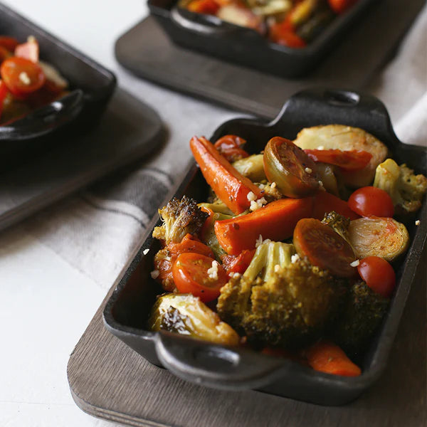 Roasted vegetables in a server dish on a wooden underliner.